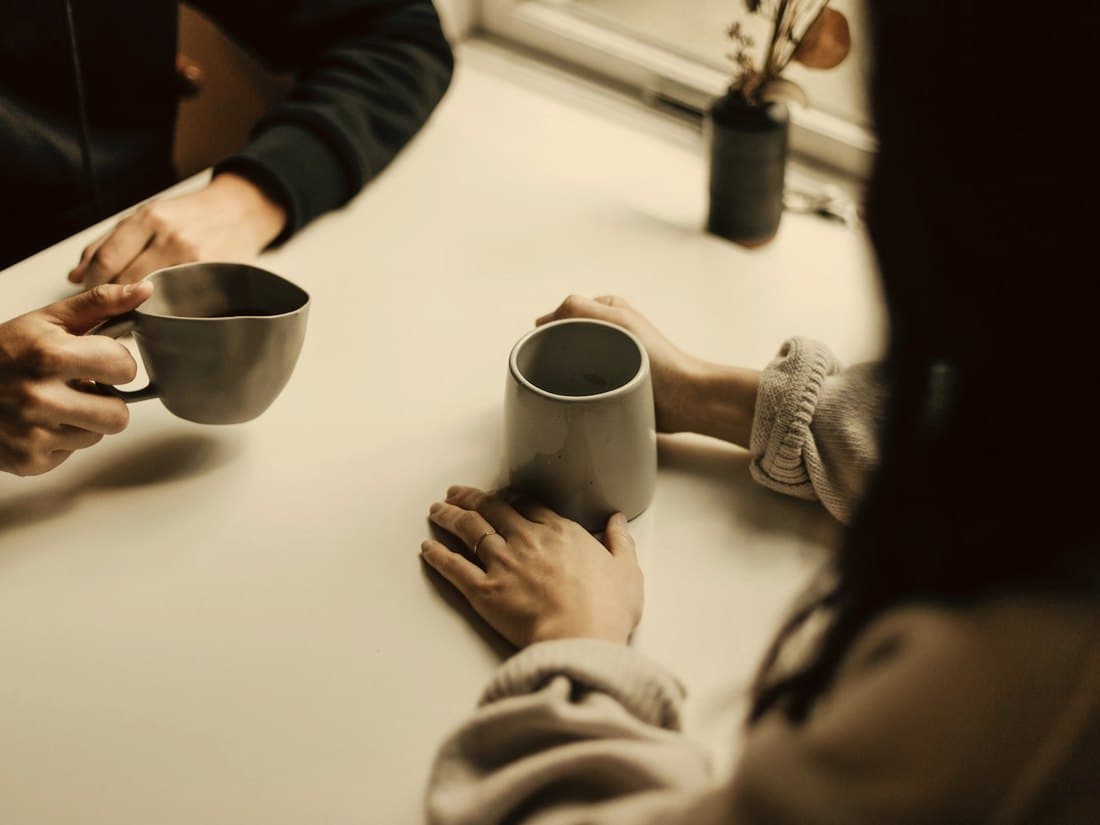 Two people talking over mugs of coffee at a table